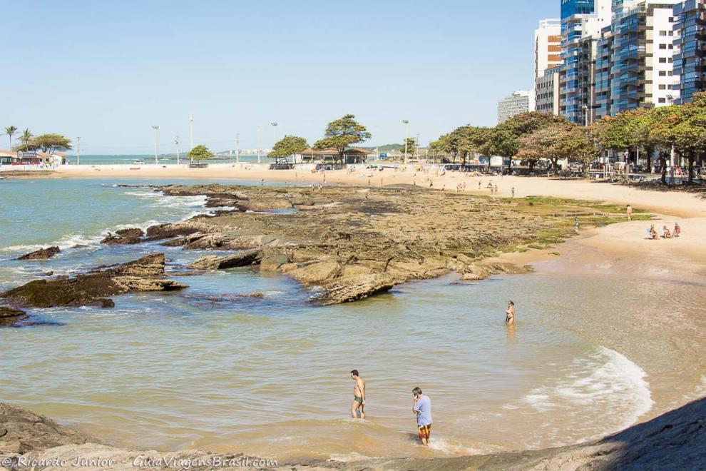 Imagem de três pessoas andando em direção ao mar da bela praia.